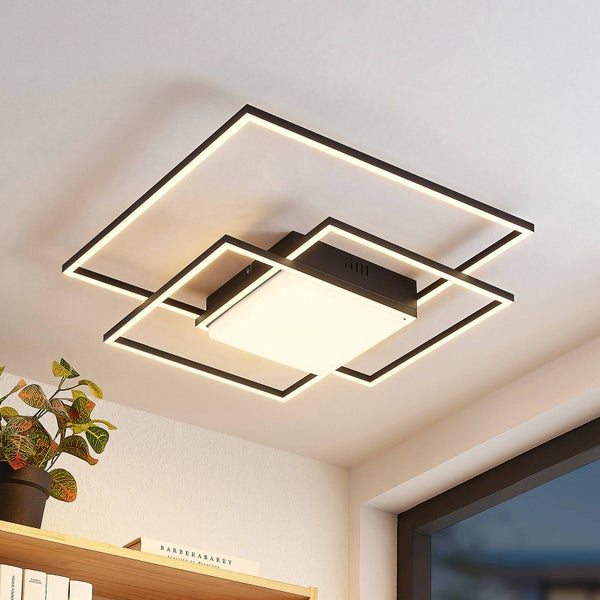 Moderne LED-Deckenleuchte aus schwarzem Metall mit quadratischen Rahmen in einem hellen Raum mit Zimmerpflanze und Bücherregal.