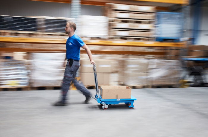 Ein Arbeiter zieht einen Transportwagen durch ein Lagerhaus.