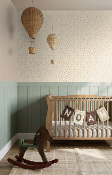 Kinderzimmer mit Holz-Babybett, grüner Wandpaneele, floraler Tapete und dekorativen Heißluftballons aus Korbgeflecht.