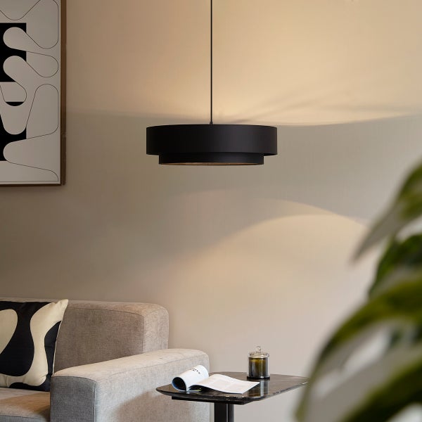 Moderne, schwarze Pendelleuchte mit zweistufigem Schirm in einem hellen Wohnzimmer über einem Beistelltisch neben einem Sofa.