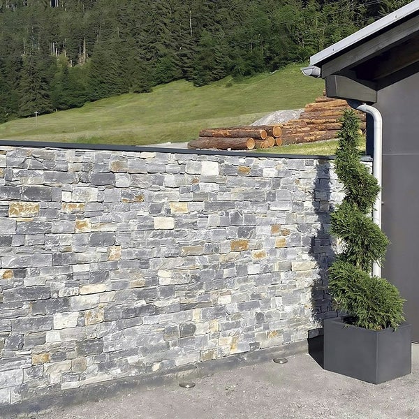 Natursteinmauer aus Schichtmauerwerk vor einer Gartenlandschaft mit einer spiralförmig geschnittenen Konifere in einem quadratischen Pflanzgefäß.