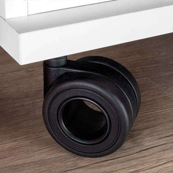 Schwarze Möbelrolle als Doppelrolle, montiert unter einem weißen Möbelstück auf einem Boden in Holzoptik.