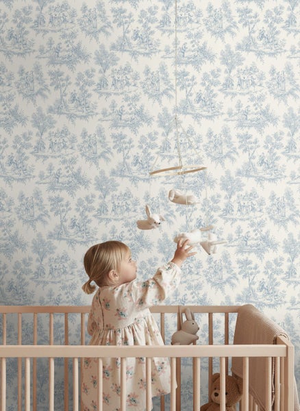 Vliestapete mit Toile-de-Jouy-Muster in einem hellen Kinderzimmer hinter einem Gitterbett aus Holz.