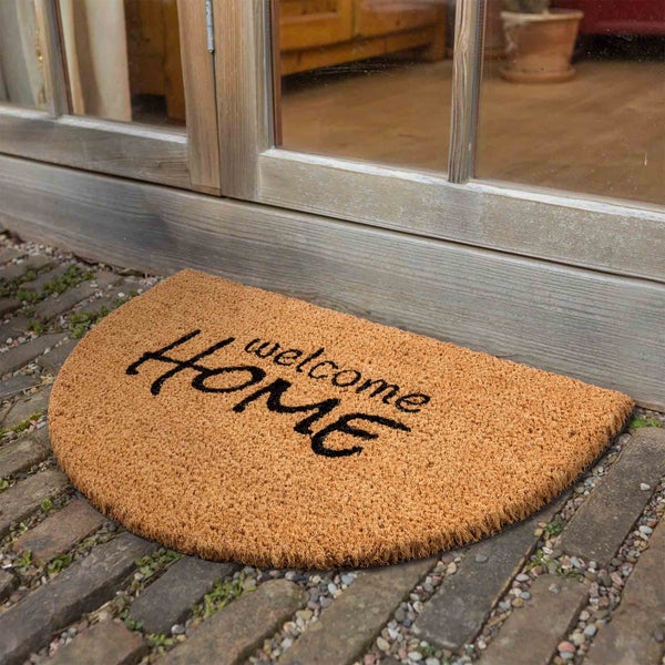 Halbrunde Fußmatte aus Kokosfaser mit der Aufschrift Willkommen Zuhause vor einer Tür