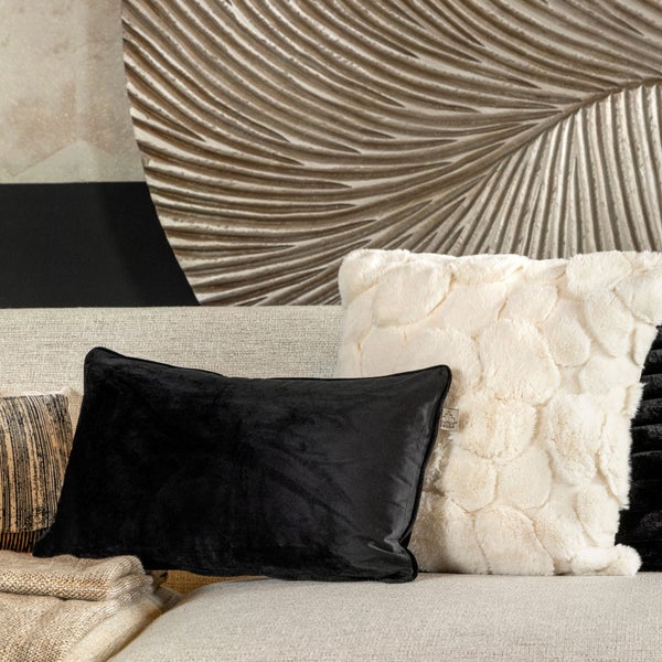 Dekorative Kissen auf einem Sofa, darunter ein schwarzes Samtkissen und ein flauschiges Kissen