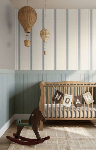 Kinderzimmer mit gestreifter Tapete, einem Babybett aus Holz, einer hölzernen Schaukelpferd-Figur und hängenden Deko-Heißluftballons aus Rattan.