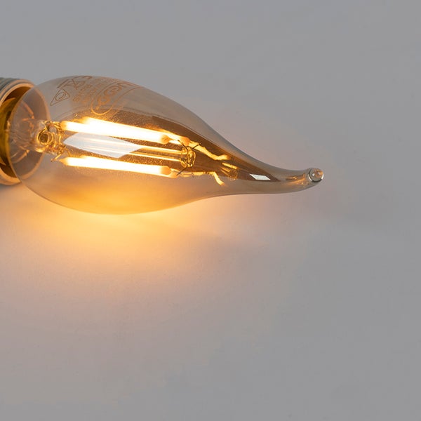 Leuchtende LED Filament Lampe in Windstoß Kerzenform mit warmweißem Licht und goldfarbenem Glas.