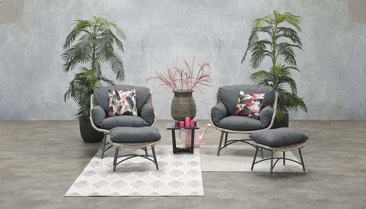 Modernes Garten-Lounge-Set mit zwei Sesseln, dunkelgrauen Kissen, zwei Hockern und einem Beistelltisch vor einer grauen Wand.