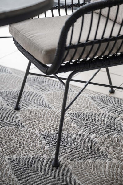 Nahaufnahme eines modernen Gartenstuhls mit schwarzem Geflecht und hellem Sitzkissen auf einem gemusterten Outdoorteppich.