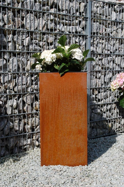 Hohe rechteckige Pflanzsäule aus Corten-Stahl mit Rost-Optik bepflanzt mit Hortensien vor einer Gabionenwand auf Kies.