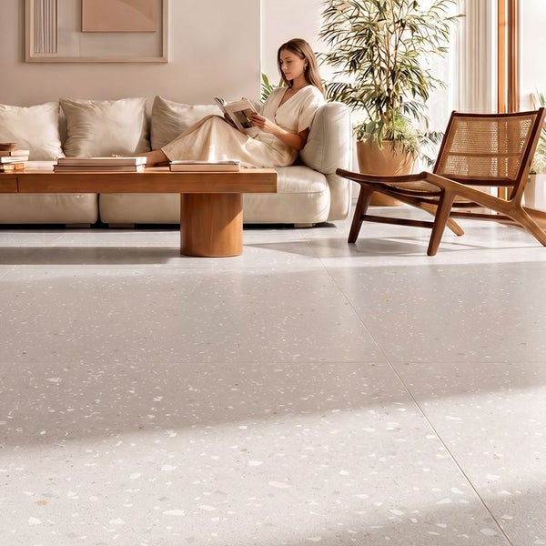 Helles Wohnzimmer mit großflächigen Terrazzo Fliesen auf dem Boden, modernem Sofa, Holztisch und einem Rattansessel in einer Wohnumgebung.