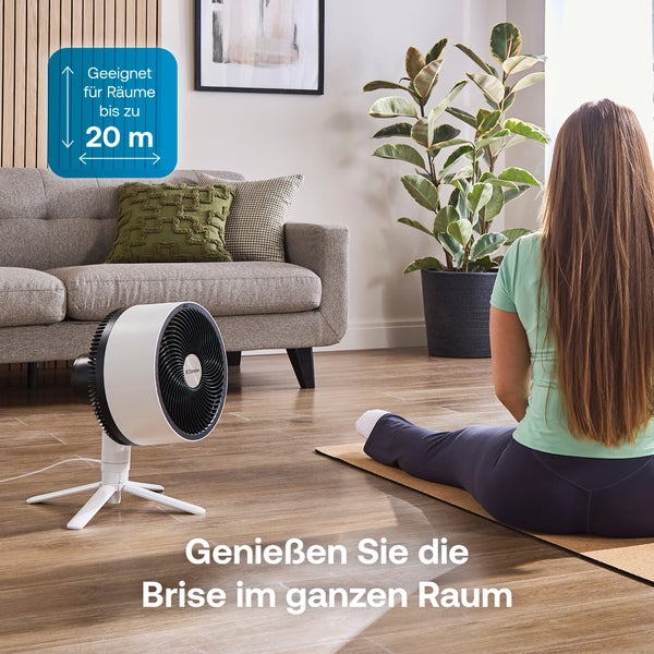 Standventilator in einem hellen Wohnzimmer mit einer Person auf einer Yogamatte, geeignet für Räume bis zu 20 Quadratmeter. Dimplex Logo.