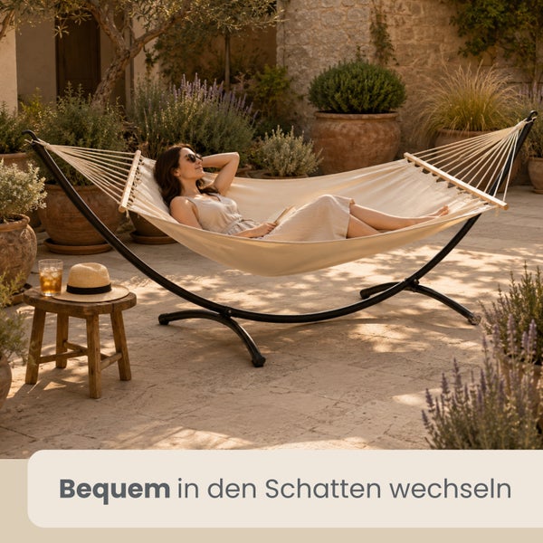 Eine Frau entspannt in einer cremefarbenen Hängematte mit schwarzem Metallgestell auf einer mediterranen Steinterrasse mit vielen Pflanzen.