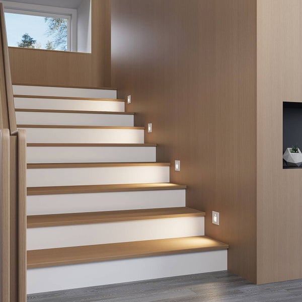 Moderne Holztreppe mit weißen Setzstufen und quadratischen LED-Wandeinbauleuchten zur Stufenbeleuchtung.