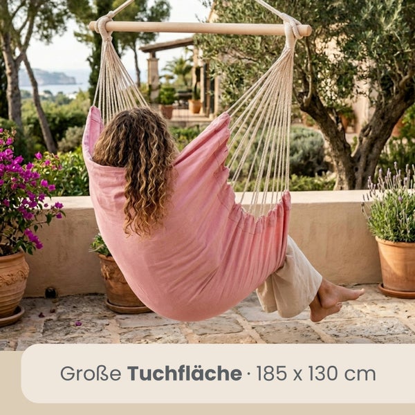 Person im rosa Tuchhängesessel mit Holzstab auf einer hellen Terrasse im Garten, Tuchfläche 185 mal 130 Zentimeter.
