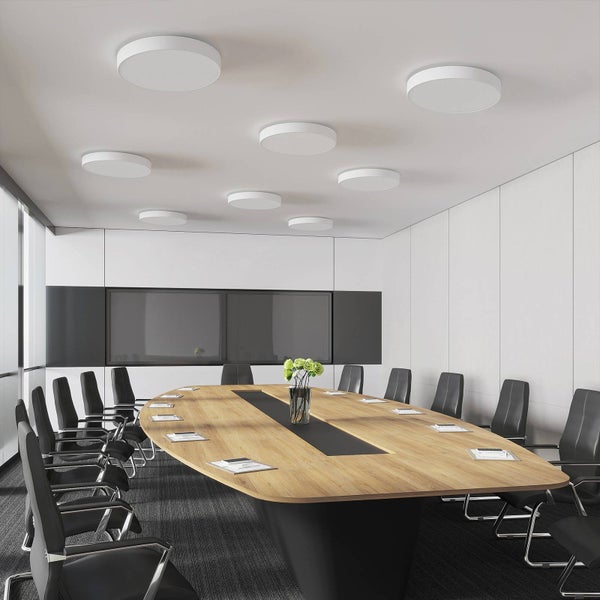 Moderner Konferenzraum mit großem ovalem Holztisch, schwarzen Bürostühlen und runden LED-Deckenleuchten in verschiedenen Größen.