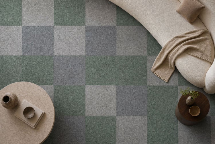 Wohnzimmer mit Teppichfliesen im Schachbrettmuster in Grau- und Grüntönen, einem runden Couchtisch und einem geschwungenen Sofa.