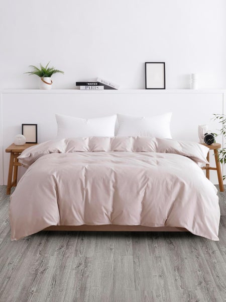 Hell eingerichtetes Schlafzimmer mit Bett, hellrosa Bettwäsche, weißen Kissen, grauem Holzboden, hölzernen Nachttischen und einem Regal.