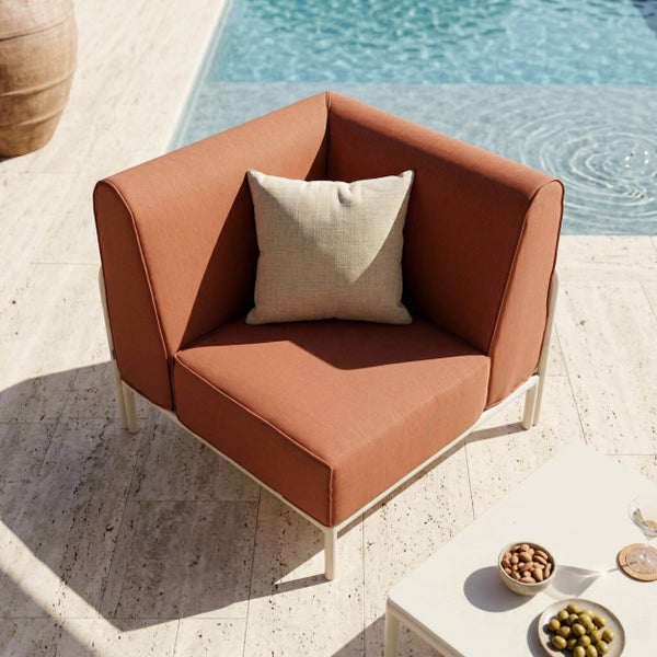 Eckelement für Gartenlounge mit terrakottafarbenen Polstern und beigem Kissen auf einer hellen Steinterrasse am Pool.