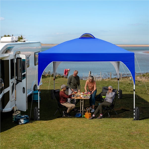 Personen sitzen unter einem blauen Pavillon neben einem Wohnmobil im Freien.