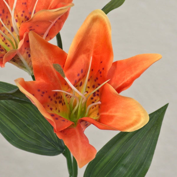 Künstliche Lilie in Orange mit grünen Blättern und dunklen Punkten auf den Blütenblättern.