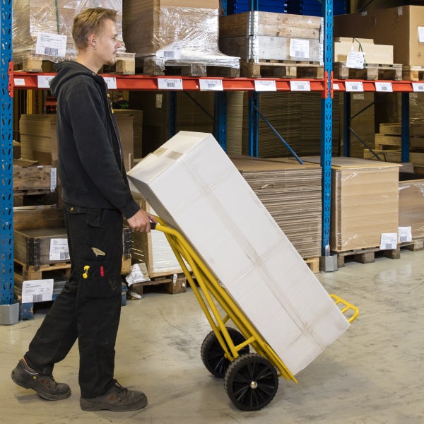 Ein Arbeiter transportiert eine große Kiste mit einer Sackkarre in einem Lagerhaus