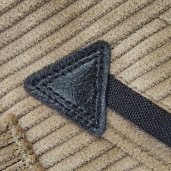 Nahaufnahme eines dreieckigen Leder-Patches mit Ziernähten auf Cordstoff und einem gewebten Gurt.
