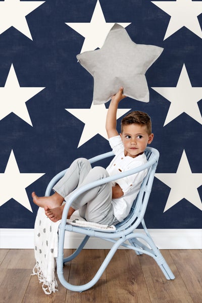 Junge sitzt in einem Sessel mit Sternenkissen vor Sternentapete
