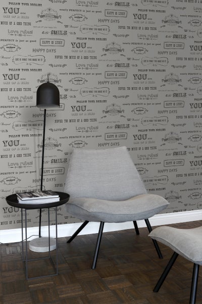 Wohnzimmer mit Tapete mit Schriftzug, Sessel, Fußhocker, Stehlampe und Beistelltisch