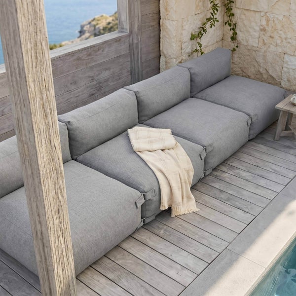 Graues modulares Outdoor-Sofa auf einer Holzterrasse an einem Pool mit einer Steinwand im Hintergrund.