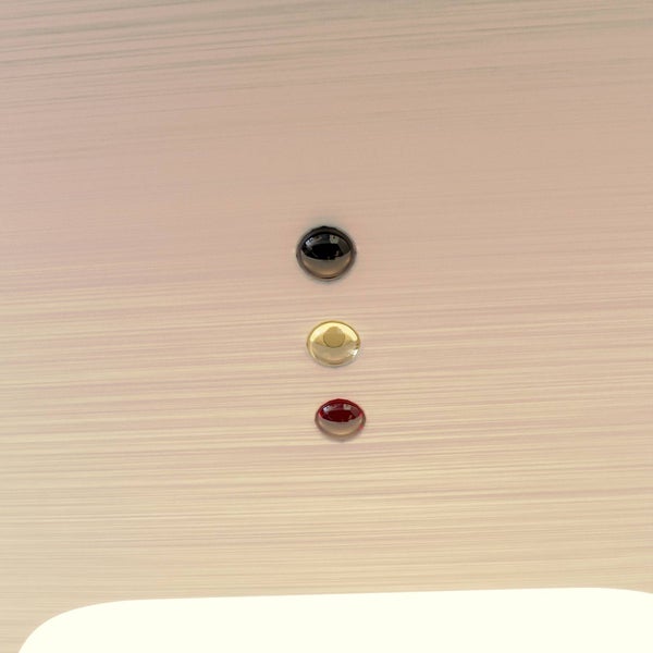 Detailaufnahme von drei runden, glänzenden Markierungspunkten in Schwarz, Gold und Rot auf einer gebürsteten, hellen Oberfläche.