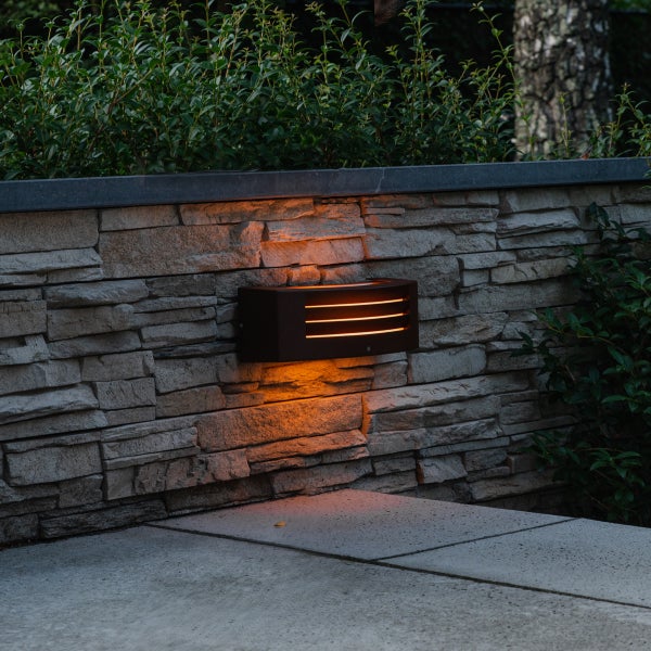 Moderne Außenwandleuchte mit warmem Licht an einer Gartenmauer aus Stein.