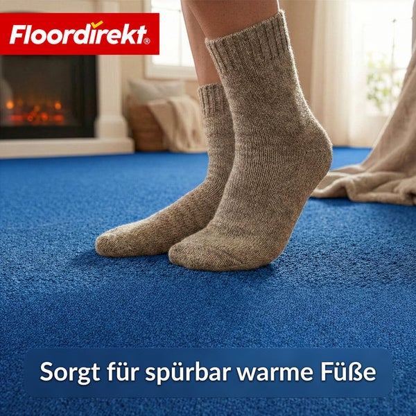 Person mit Socken auf blauem Teppichboden vor Kamin und Fenster. FloorDirekt Logo.