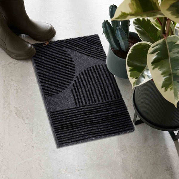 Schmutzfangmatte mit Muster, Gummistiefel und Zimmerpflanzen auf dem Boden.