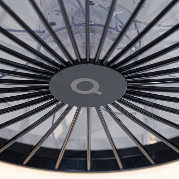 Nahaufnahme eines Deckenventilators mit radialem Schutzgitter, transparenten Flügeln und Q Logo in der Mitte.