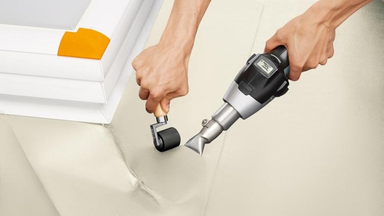 Verschweißen einer Dachfolie mit einem Heißluftgebläse mit Digitalanzeige und einer Andrückrolle an einem Dachfensterrahmen.