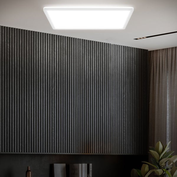 Rechteckiges LED-Panel an einer weißen Decke über einer dunklen Wand mit Holzlamellen in einem modernen Zimmer.