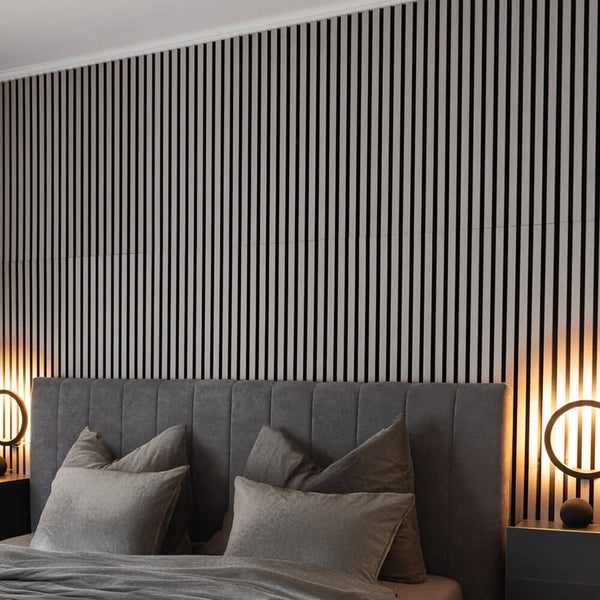 Akustikpaneel mit vertikalen Holzlamellen an einer Wand hinter einem gepolsterten Bett in einem modern eingerichteten Schlafzimmer.
