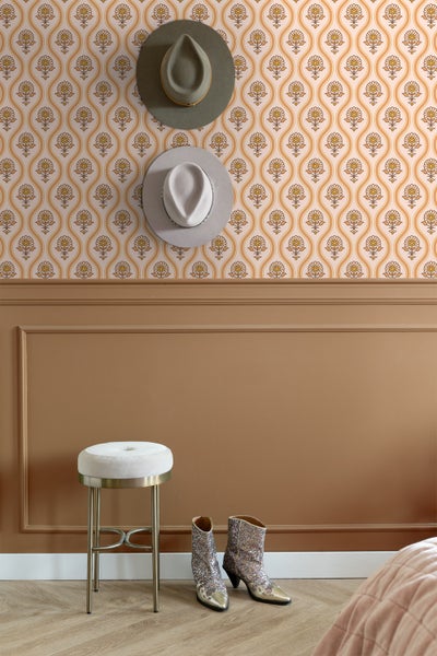 Szene mit floral gemusterter Tapete, zwei Hüten an der Wand, einem Hocker und glitzernden Cowboystiefeln.