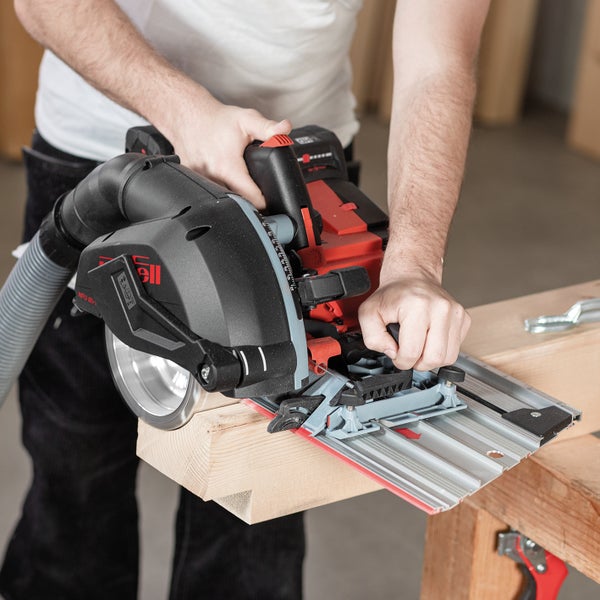 Person führt eine Mafell NFU 50 Fräse mit Führungsschiene auf einem Holzbalken, verbunden mit einer Absaugung zur Holzbearbeitung.