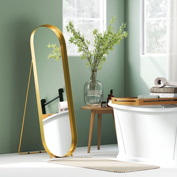 Badezimmer mit freistehender Badewanne, Standspiegel mit goldfarbenem Rahmen und Beistelltisch mit Vase und Dekoration