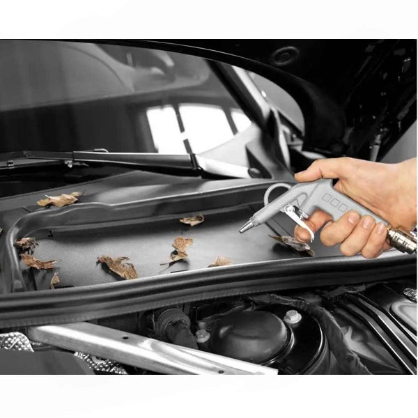 Eine Hand verwendet eine Druckluft-Ausblaspistole, um trockenes Laub aus dem Bereich unter der Windschutzscheibe eines Autos zu entfernen.