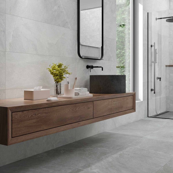 Modernes Badezimmer mit grauen Fliesen in Steinoptik, schwebendem Holzwaschtisch, dunklem Steinwaschbecken und gläserner Duschkabine.