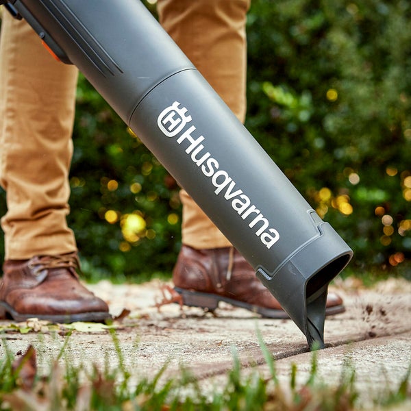 Person verwendet Laubbläser der Marke Husqvarna zur Reinigung von Pflastersteinen