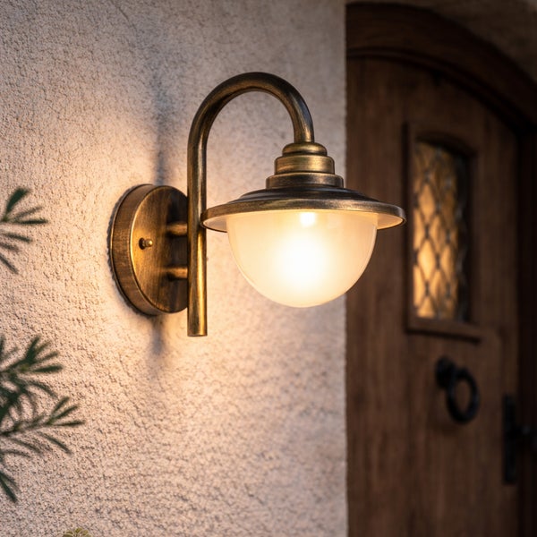 Außenwandleuchte in antikem Messing-Design mit rundem Schirm aus Glas, montiert an einer weißen Hauswand neben einer Holztür.