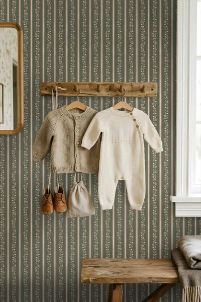 Tapete mit vertikalen Streifen und floralem Muster in einem Kinderzimmer mit Holzgarderobe, Babykleidung und Spiegel.