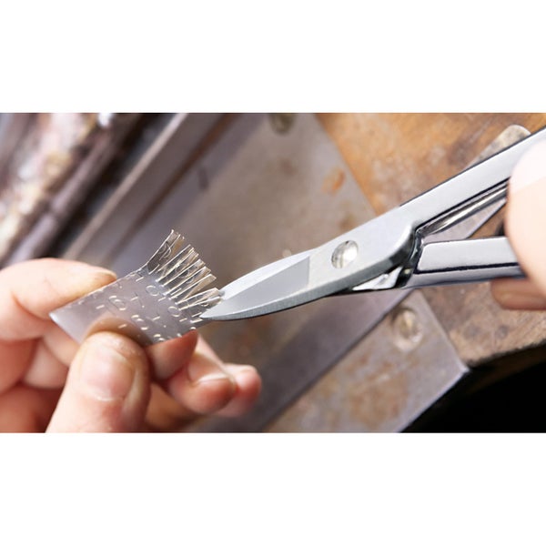 Hände schneiden einen dünnen Metallstreifen mit Markierungen mit einer Metallschere auf einer Werkbank.