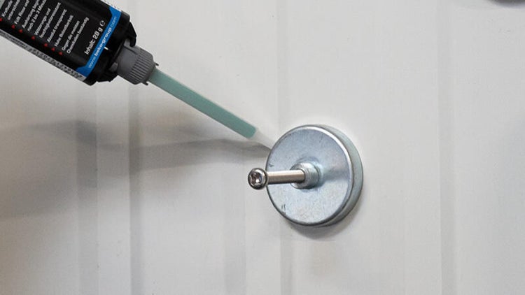 Klebemasse wird auf einen Metallhaken aufgetragen