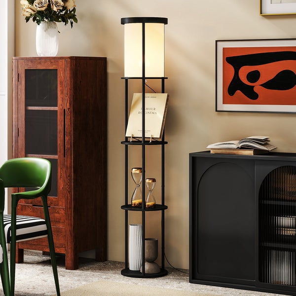 Moderne Stehleuchte aus schwarzem Metall mit runden Ablagefächern in einem hellen Wohnzimmer mit Holzschrank und grünem Stuhl.