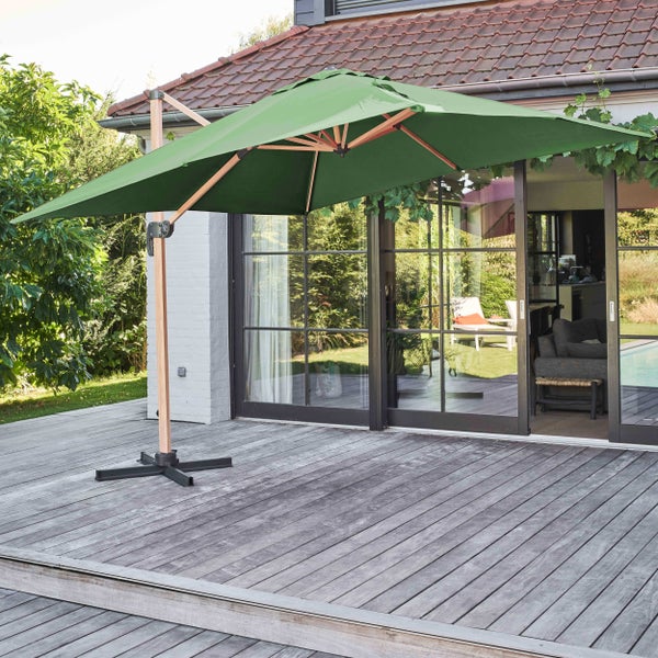 Grüner Ampelschirm mit Holzgestell auf einer weitläufigen Holzterrasse vor einem hellen Wohnhaus mit moderner Glasfront.